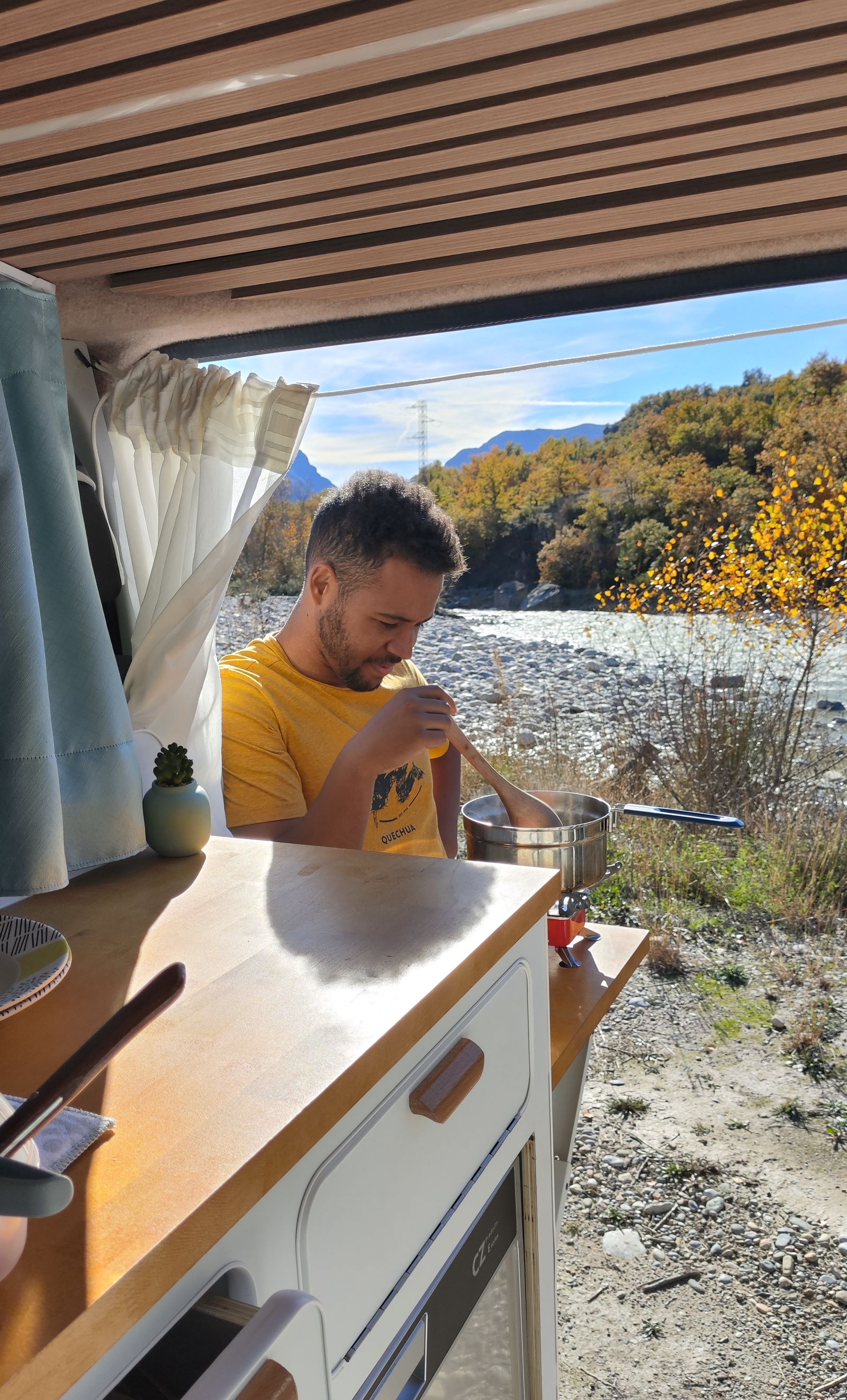 Gerard cocina en la encimera con la puerta lateral abierta a la orilla de un río en otoño.